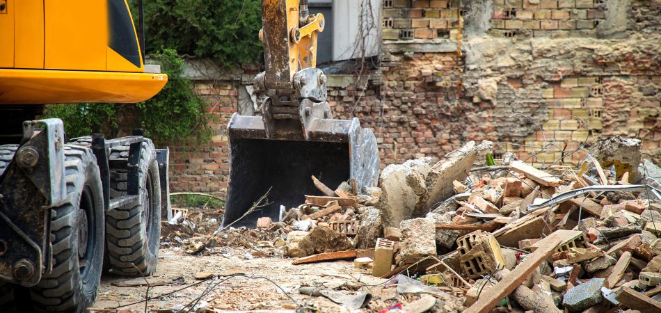 An excavator picking up rubble outside of a house being demolished.
