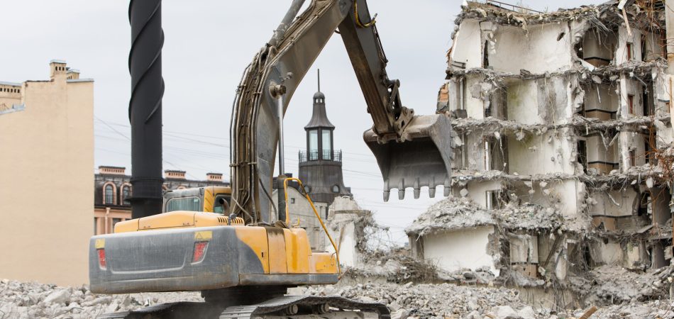 A yellow excavator picking up rubble on top of a building