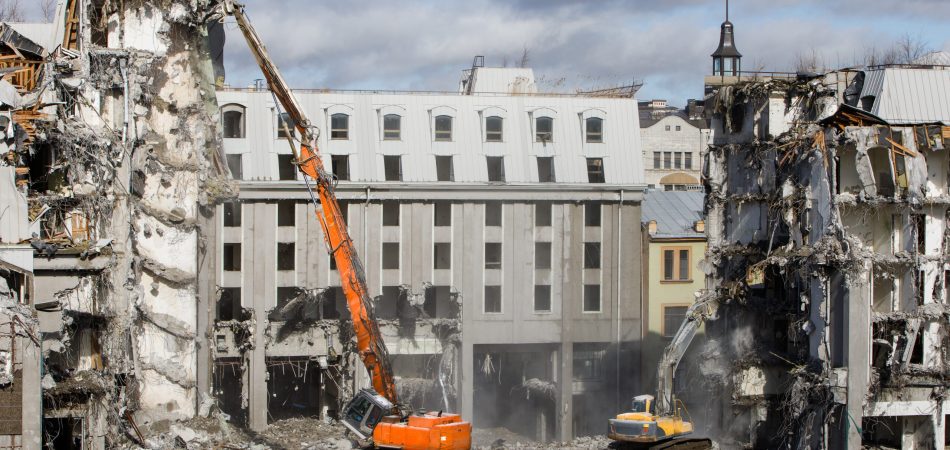 Three buildings in the process of being demolished with a crane.
