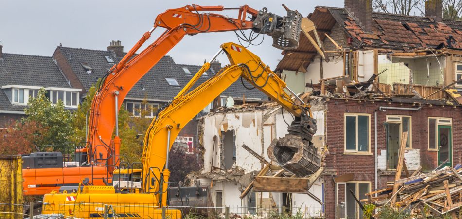 Two demolition cranes breaking a home down a house